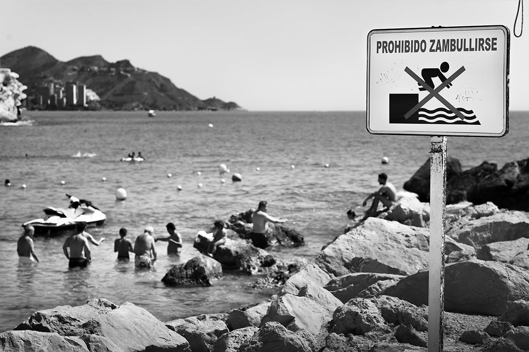 Bathers among rocks beneath a no-diving sign.